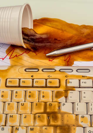 in an office, a cup spilling coffee on a computer by accidentの写真素材