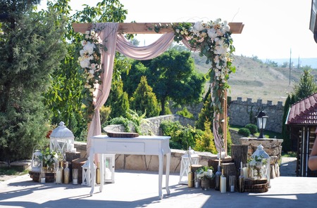 Beautiful wedding ceremony outdoors. Wedding arch made of cloth and white and pink flowers on a green natural background. Old doors, rustic style.の写真素材