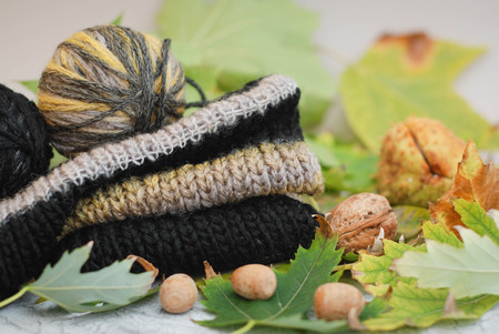 Autumn still life - Warm knitted scarf, on wooden table with fall leaves. Knitted sweater with autumn leaves and nuts. Autumn cozy background. Top view.の写真素材
