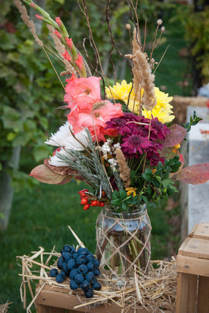 Bunch of colorful autumn flowers in glass jar with grapeの写真素材