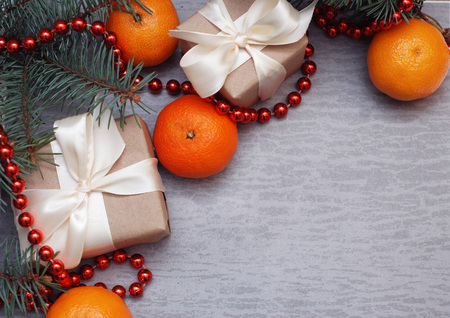Christmas Gift Box with White Ribbon and Craft Paper. Cristmas Concept, Tangerine, fir Branches and Red Beads on Gray Background.の写真素材