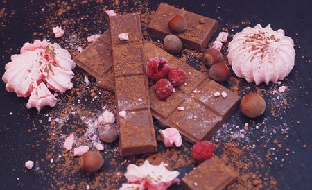 Chocolate bar pieces and cubes on darck background, top view with Meringues and Raspberriesの写真素材
