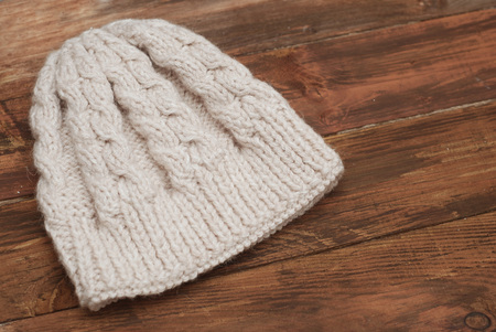 Close-up of beautiful warm ivory knitted hat. Knitted warm handmade hat with beautiful ornament on wooden background.の写真素材