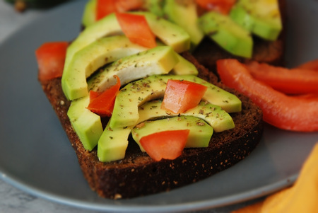 Vegetarian healthy wholegrain bread with avocado and cherry tomatoes on gray plate woth orange napkinの写真素材