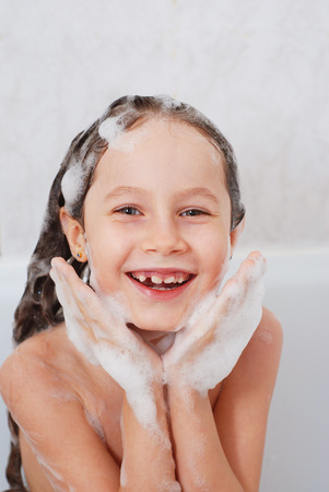 A Happy Little Beautiful Girl Smiling Washing Her Hair in Bathroom with Water and Foam. Vertical Portret.の写真素材