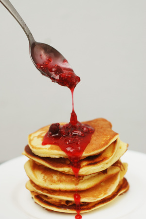 Strawberry Jam Pouring over a Stack of Pancakes. Snack of pancakes of jam on rustic white table.の写真素材