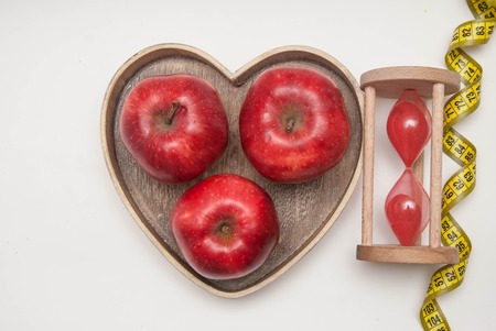 Healthy Food Concept. Diet and Fitness. Glass Clock and Red Apple in Heart Shape Wooden Box. Measuring Tape, isolated on white background with copy space. flat Lay.の写真素材