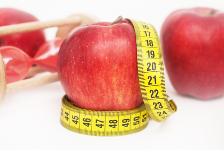 Lose Weigh. close Up of Measuring Yellow Tape Ties Around Red Apple with Glass Sand Clock Isolated on white background. horizontal image with copy space for Text.の写真素材