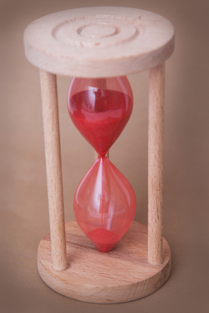 Red Hourglass as Time passing concept and running out of time. Sandglass. Neutral Ivory Background....