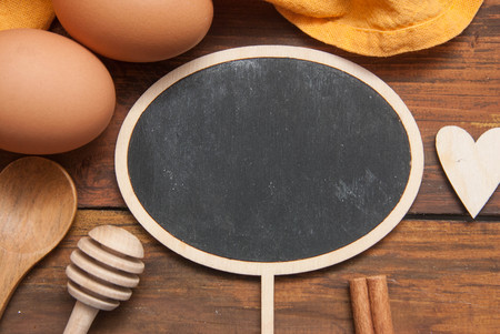 Close Up Cholkboard Topper for Text Mesage. Cooking Process, Food and Recipe Concept. Orange Napkin, Eggs, Heart Shape over Textured Rustic Wooden Table.の写真素材