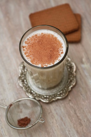 Cinnamon Powder into Glass of Milk with Biscuits over Rustic Background.の写真素材