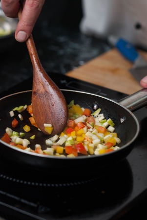 Mixing Sliced Vegetables in a Pan with Wooden Spoon on Kitchen Table.の写真素材