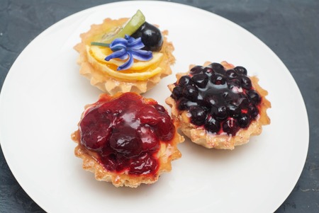 Three Tartlets with Raspberries on White Plate over Dark Backgroundの写真素材
