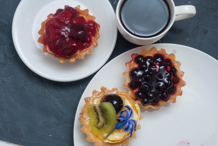 Assorted Fruit Tarttlets, or Basket, Cakes with Cream and Berries on White Plate with cup of coffee over Gray Background for holiday. Flat Lay.の写真素材