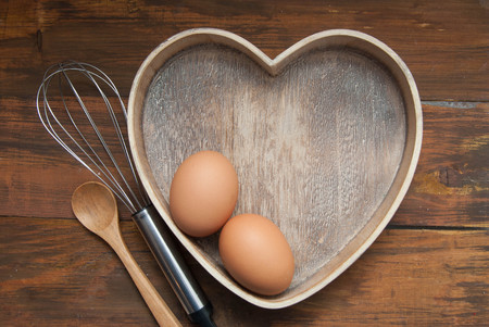 Baking tools with Wooden Heart Shape box with Eggs. Bake or food Background. Dark rustic Wooden Background with copy space. Flat Lay.の写真素材