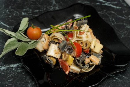 Colorful Pasta with Sauce, olivevs, Tomatoes in Black Plate. top view. food. Heart-Shaped Macarons on Black Table.の写真素材
