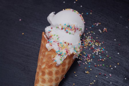 Ice Cream in waffle Cone of Vanilla ice cream and Confetti isolated on Dark Black Textured Background. Party, dessert.の写真素材