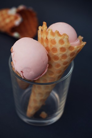Ice Cream in waffle Cone with scoop of Pink Fruit ice cream and Confetti in glass isolated on Dark blue Background.の写真素材