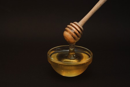 Honey in Glass bowl with dipper over dark Background Isolatedの写真素材