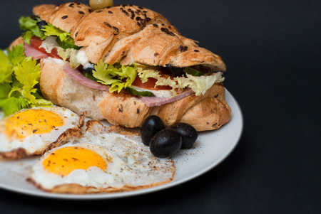 Breakfast on White Plate with Fried Eggs and Croissant with Fresh Vegetables over Black Background. Food conceptの写真素材