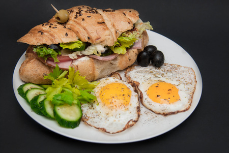 Breakfast on White Plate with Fried Eggs and Croissant with Fresh Vegetables over Black Background. Food conceptの写真素材