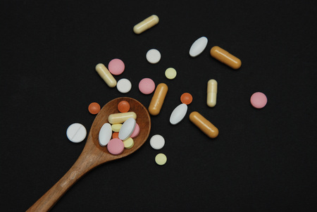 Colored Pills in Wooden spoon with a portion of medicine Pills isolated on Black Background. Medicine concept.の写真素材