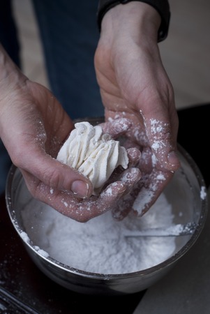 Woman's hands Sprinkling with Icing Sugar a Zephyr . Confectioner Sprinkles Powdered Sugar on White Marshmallowの写真素材
