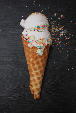 Ice Cream in waffle Cone of Vanilla ice cream and Confetti isolated on Dark Black Textured Background. Party, dessert.の写真素材