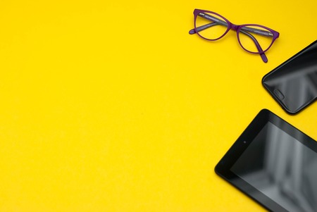 Eyeglasses on Ipad and Mobile Phone over Yellow Background with copy space.