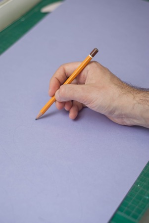 Human Men's Hand Holding a simple Pencil over Purple Paper.の写真素材