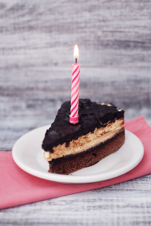 Chocolate Cake with Candle. Piece of Desert Birthday Cake Isoalted on gray Woden Table
