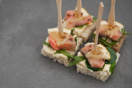Salmon Canape with Arugula Leaves, butter Cream and White Bread. Healthy Snack. Gray Background.
