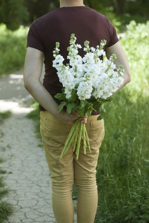 Young Man Holding White Flower bouquet at his Back. Wooden brown background.の写真素材