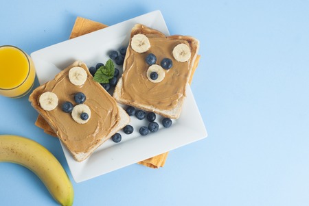 Breakfast Toast Bear Shaped Peanut Butter Banana Bread Blueberry for Kids. Funny animal face toast for kids snack. Blue Background.の写真素材