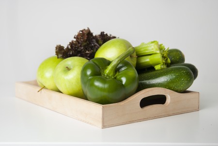 Fresh green vegetables and fruits in wooden boxes on white background. Bell pepper, apples, zucchini, celery, salad leaves.の写真素材