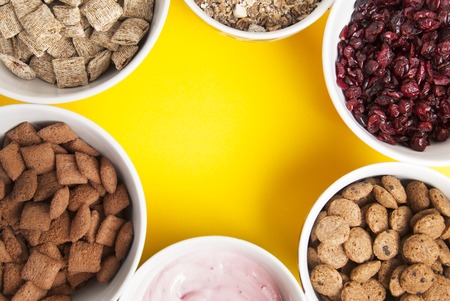 Bowls of whole grain muesli, dried fruits, granola and oatmeals arranged in circle with copy space in centre. Isolated on yellow background.の写真素材
