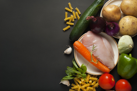 Raw chickenbrest with ingredients, vegetables for cooking on a black backgroundの写真素材