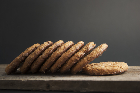 Oatmeal cookies or biscuits with oats, nuts, eggs and flour on brown dark woodenboard with black background, isolated.の写真素材