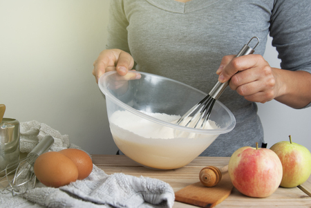 Close-up young woman's hands holding whisk and bowl while making pie, cake. Female cooking dough for pie on wooden table. Preparring dessert. Isolated.の写真素材