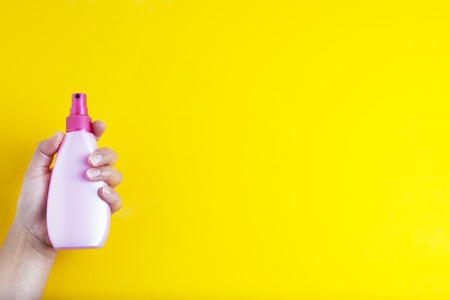 Hand holding pink spray cosmetic plastic bottle, isolated on yellow backgroundの写真素材