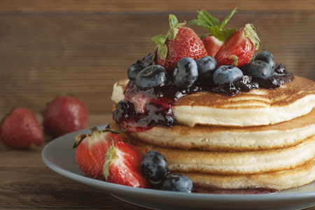 American pancakes or fritters served with strawberry and blueberry jam, delicious dessert for breakfast, rustic style.の写真素材