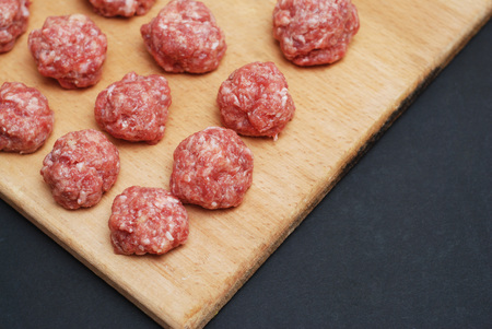 Raw Balls from Raw Beef Meat on Wooden Board over Dark Background