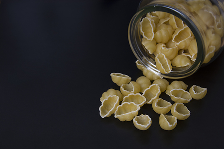 Unooked fonchiglie pasta isolated.Yellow raw macaroni or pasta over black board.