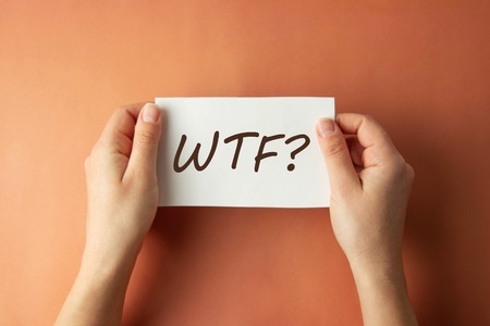 WTF inscription. Woman holding paper with WTF lettering in hands isolated brown background.の写真素材