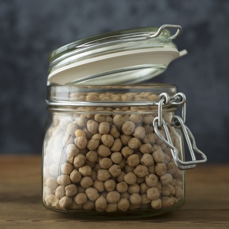 Dried chickpeas in glass jar on wooden background with copy space. Isolated.の写真素材