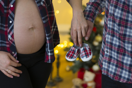 Future parents holding hands and a pair of little shoes over christmas backgroundの写真素材