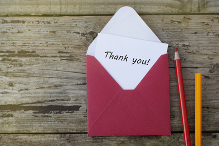 Thank you inscription - red envelope with blank card on wooden background with copy space, and red pencils.の写真素材