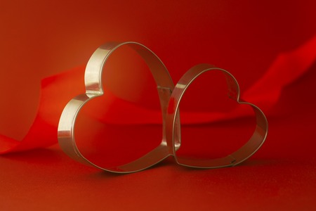 Happy Valentine's Day inscription. Greeting card. Two red heart shaped cookie cutters on beautiful red background.の写真素材
