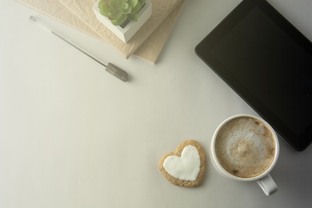 Flat lay of work desktop with coffee cup or latte, notepad with notebook.