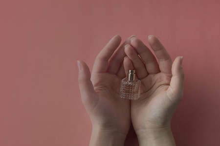 Female perfume in hands on pink